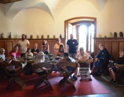 Mehrere Kinder und Betreuerinnen sitzen in einem Saal mit hohen Wänden.