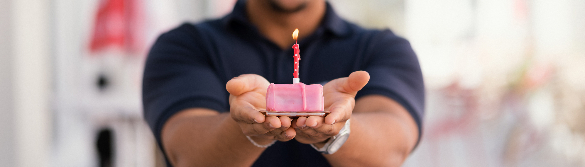 Mitarbeiter vom Samariterbund Wien hält eine Kleine Torte mit Kerze in den Händen und lächelt