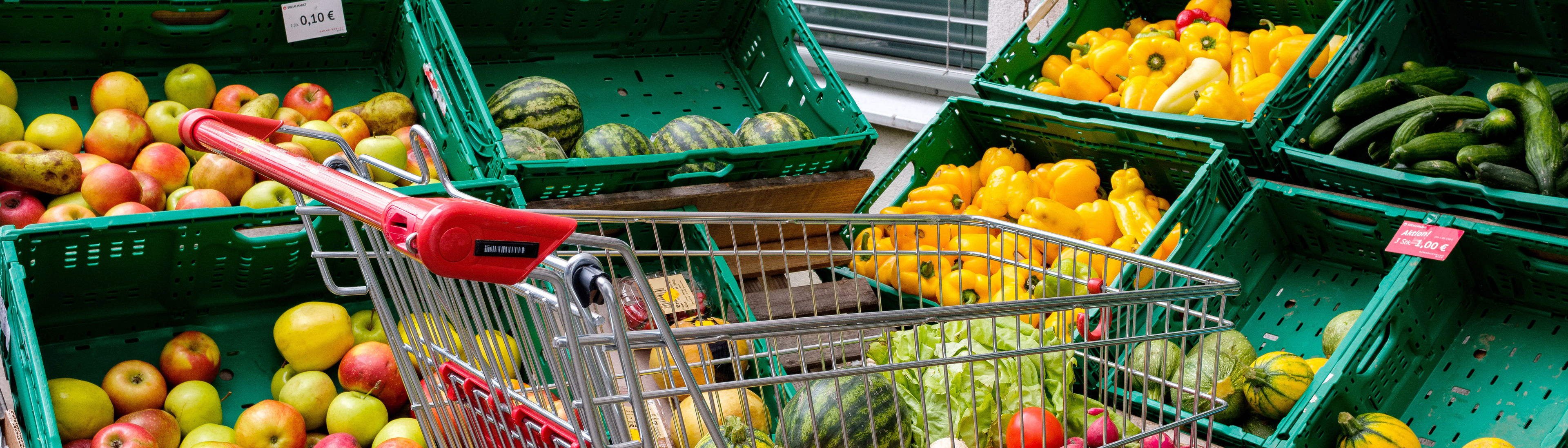 Sozialmarkt - Befüllter Einkaufswagen vor Obst- und Gemüseregal