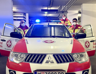 zwei Rettungssanitäterinnen mit Maske, bei Rettungsauto, geöffnete Türen, stehen dahinter 