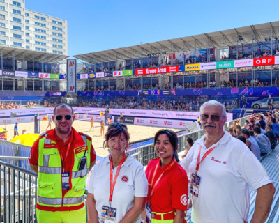 Gruppenbild Sanitäter:innen beim Sanitätsdienst beim Beachvolleyball EM in Wien, im Hintergrund Volleyball Court mit Zuschauertribünen