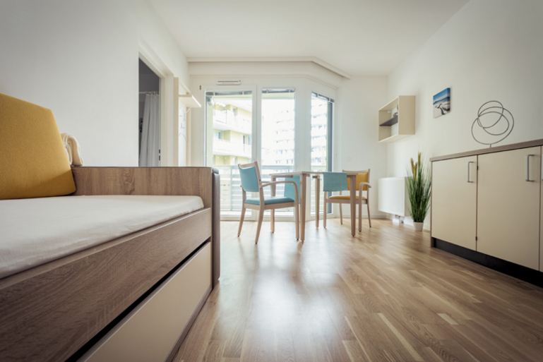 Senioren-WG Braunhubergasse Ansicht eines Einzelzimmers mir Bett, Tisch und Sideboard