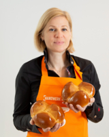 Frau mit orangener Schürze von Bäckerei Szihn hält zwei Osterpinzen in der Hand und blickt in Kamera