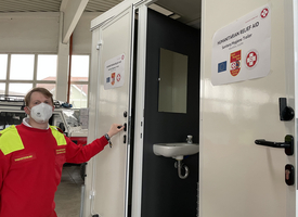 Ein Sanitäts- und Hygienetrailer mit einem Helfer im roten Outfit.