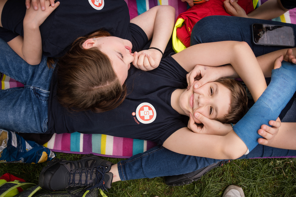 Drei Kinder in T-Shirts machen lustige Gesichter und liegen zusammen auf einer Decke.