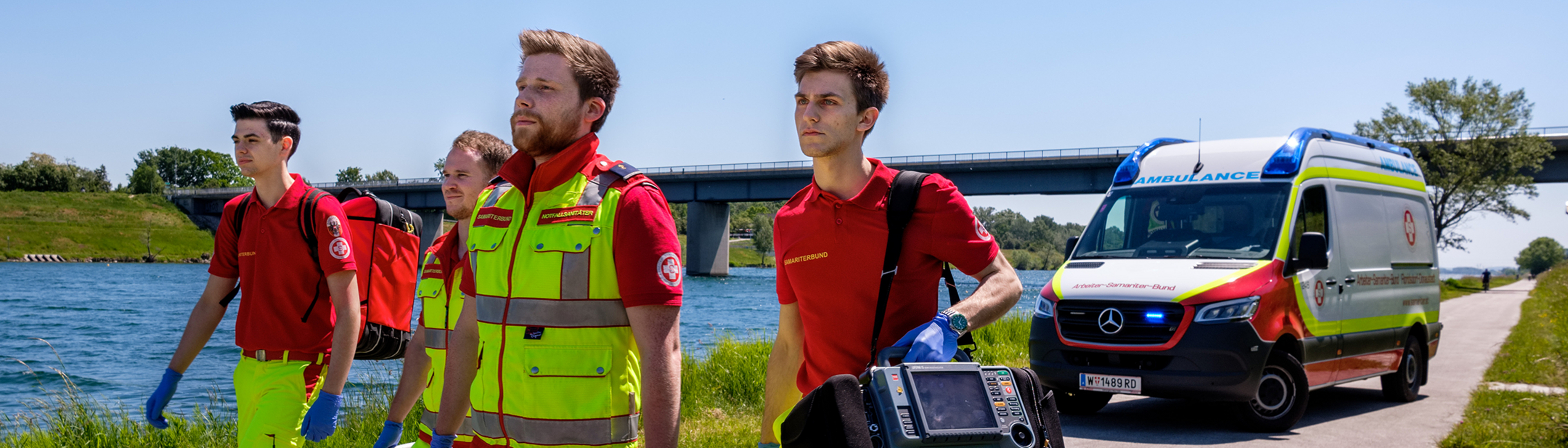 Sanitäter des Samariterbundes im Einsatz auf der Donauinsel. Im Hintergrund ist ein Einsatzfahrzeug und die Donau zu sehen.