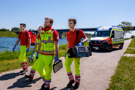 Sanitäter des Samariterbundes im Einsatz auf der Donauinsel. Im Hintergrund ist ein Einsatzfahrzeug und die Donau zu sehen.