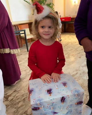 Ein kleines Mädchen in einem roten Kleid hält ein weiß verpacktes Geschenk fest.