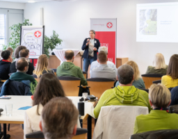 Gruppe von Menschen sitzen bei Vortrag, eine Vortragende