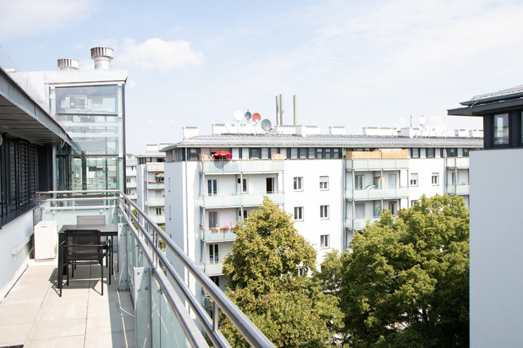 Blick von einem Balkon auf umliegende Wohnhäuser und Bäume.