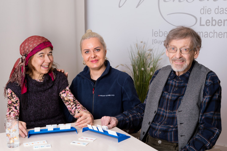 Senioren-WG Braunhubergasse zwei Bewohnerinnen und Heimhelferin lächeln in die Kamera und sitzen am Tisch