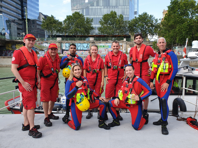 Ein Team von Rettungsschwimmern in rot-blauer Kleidung posiert am Wasser.