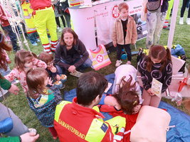 Kinder lernen beim Tag des Samariterbundes Erste Hilfe mit einer Dummy-Puppe und Samariterbund Mitarbeiter:innen.