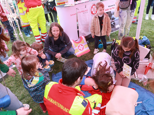 Kinder lernen beim Tag des Samariterbundes Erste Hilfe mit einer Dummy-Puppe und Samariterbund Mitarbeiter:innen.