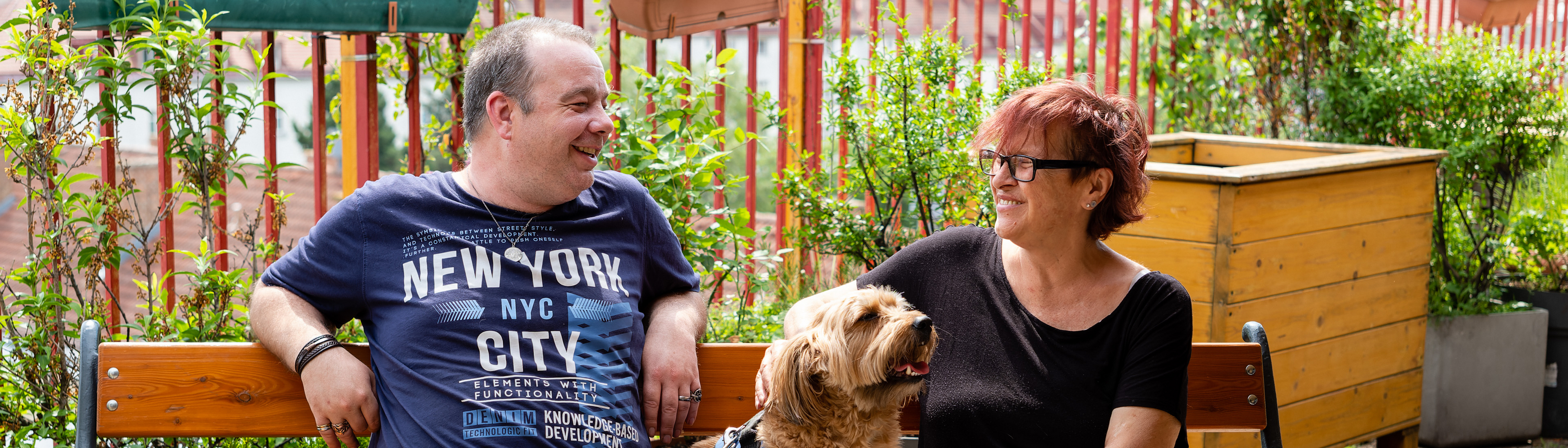 Wohnungslosenhilfe - zwei Bewohner einer Einrichtung sitzen mit Hund auf Bank, auf Terrasse