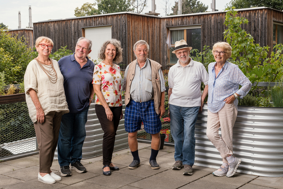 Eine Gruppe von glücklichen Bewohnerinnen und Bewohnern der Senioren-Wohngemeinschaft Mühlgrundgasse stehen im Garten